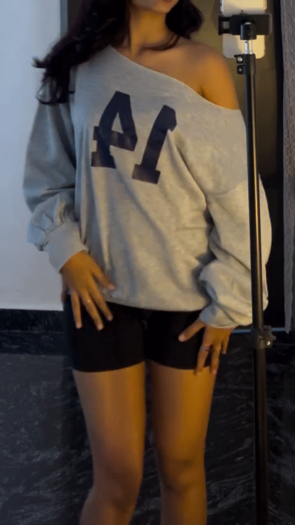 loose, off-shoulder grey sweatshirt with a large printed number on the front, paired with black fitted shorts.