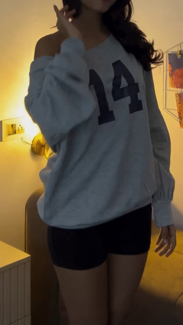loose, off-shoulder grey sweatshirt with a large printed number on the front, paired with black fitted shorts. - Image 2